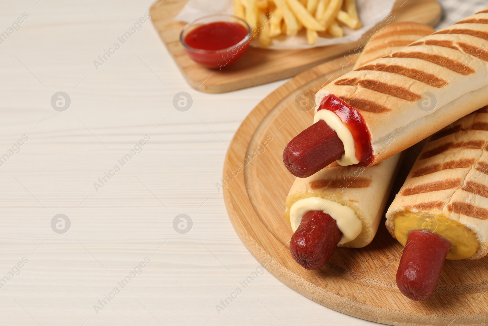 Photo of Delicious french hot dogs, fries and dip sauce on white wooden table. Space for text