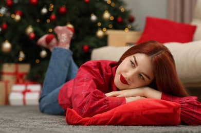 Photo of Beautiful young woman lying on floor near Christmas tree at home