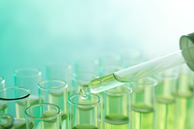 Photo of Dropping sample into test tube with liquid on color background, closeup