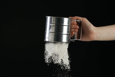 Woman sieving flour against black background, closeup. Space for text