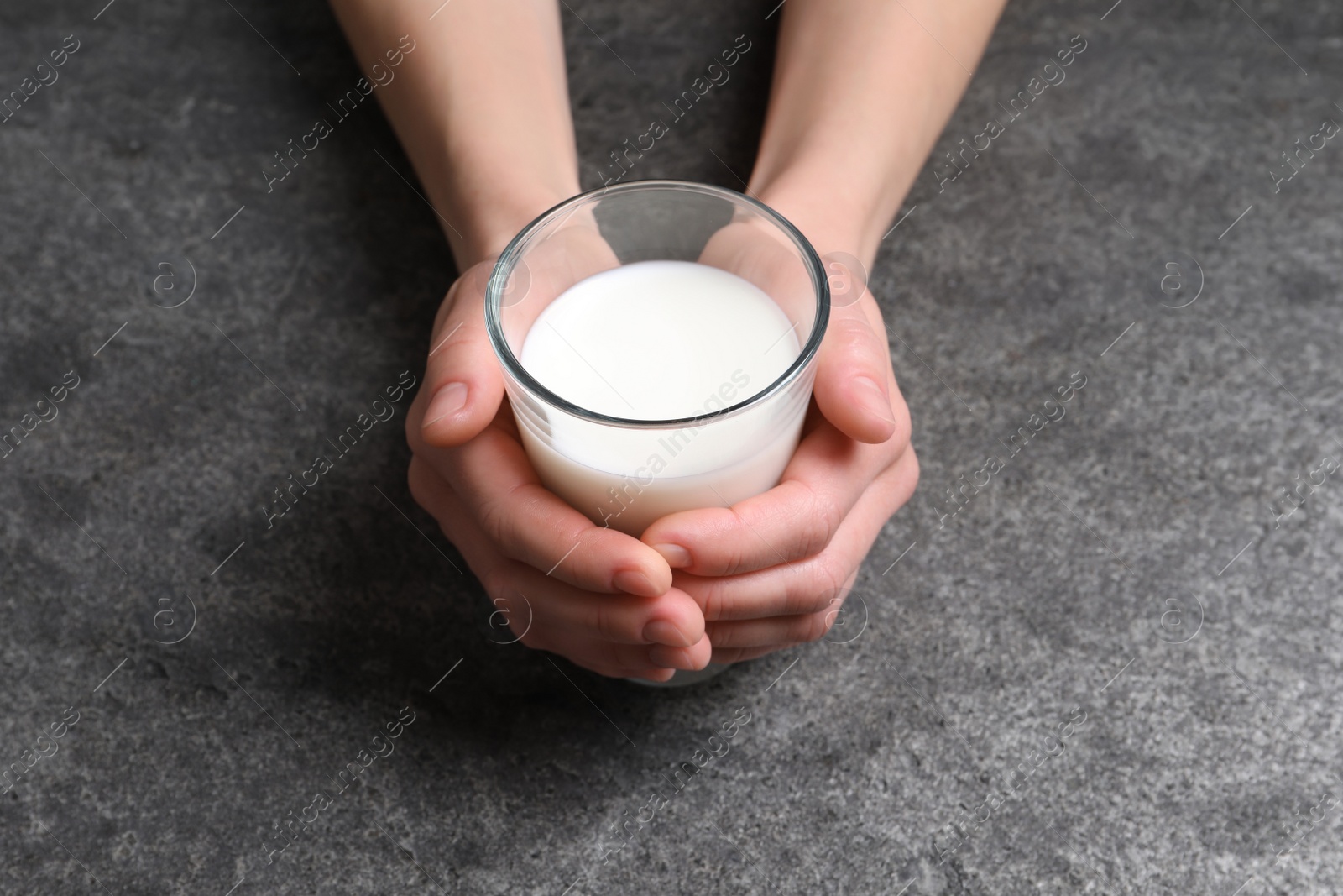 Photo of Woman holding glass of milk at grey table, closeup