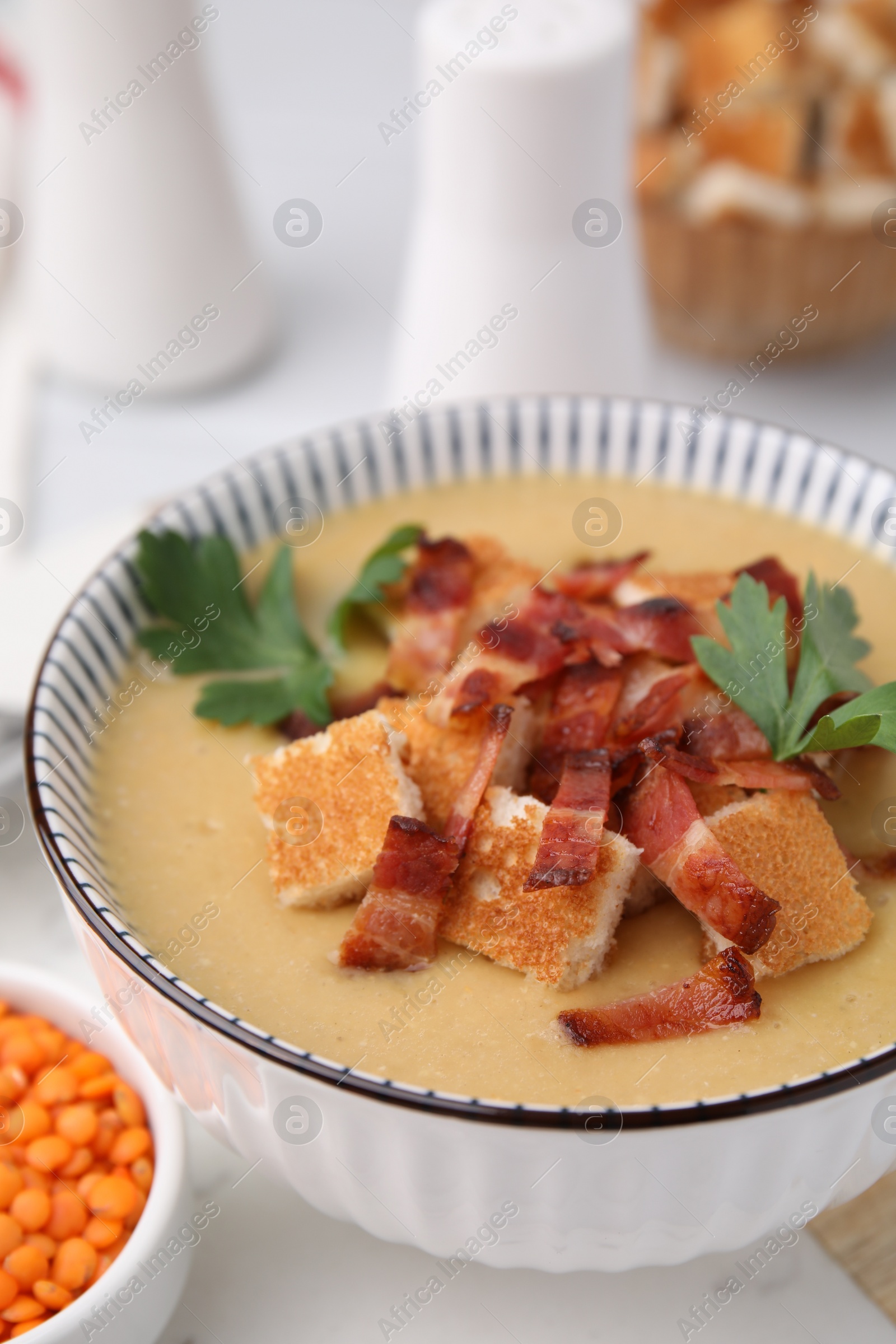 Photo of Delicious lentil soup with bacon and parsley in bowl on table, closeup