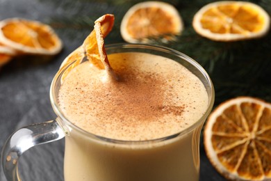 Photo of Glass cup of delicious eggnog with dried orange slice on gray table, closeup