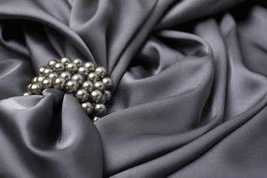 Photo of Beautiful pearls with grey silk as background, closeup. Space for text
