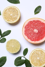 Different cut citrus fruits and leaves on white table, flat lay