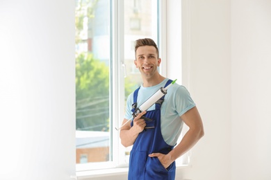 Photo of Construction worker in uniform with window sealant indoors