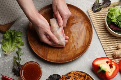 Photo of Woman making tasty spring roll at grey table, top view