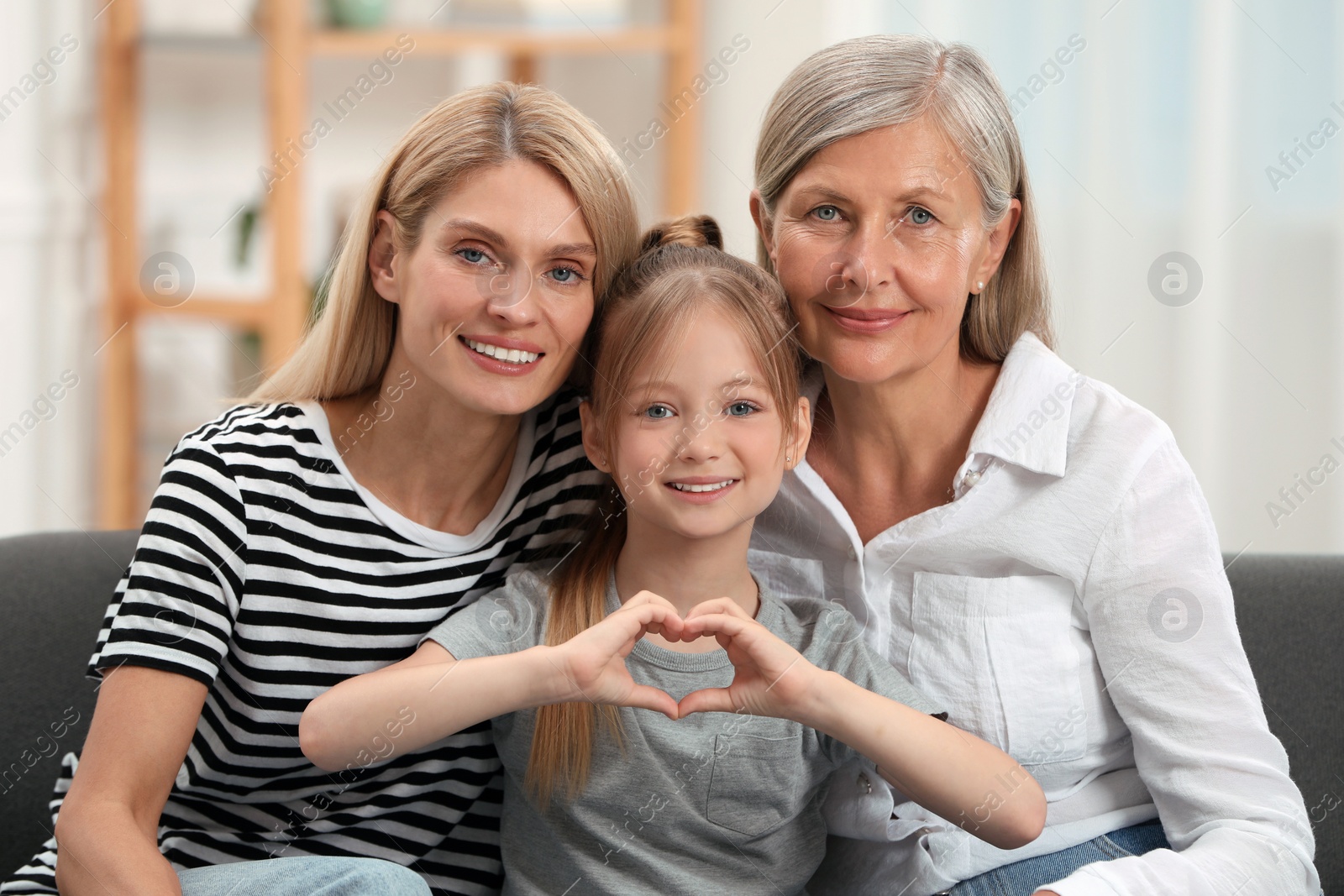 Photo of Three generations. Happy grandmother, her daughter and granddaughter making heart with hands at home