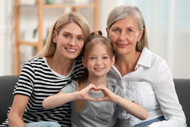 Photo of Three generations. Happy grandmother, her daughter and granddaughter making heart with hands at home