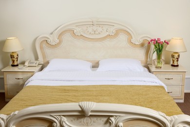Photo of Comfortable bed and beautiful bouquet on bedside table in room. Stylish interior