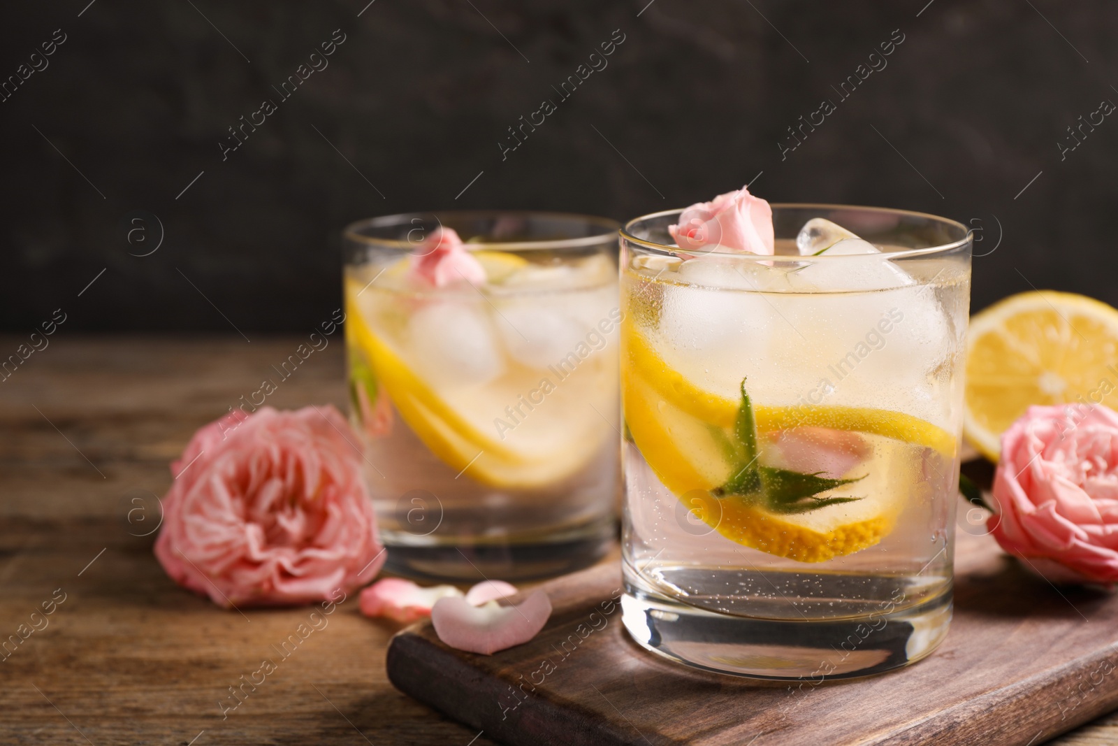 Photo of Delicious refreshing drink with lemon and roses on wooden table