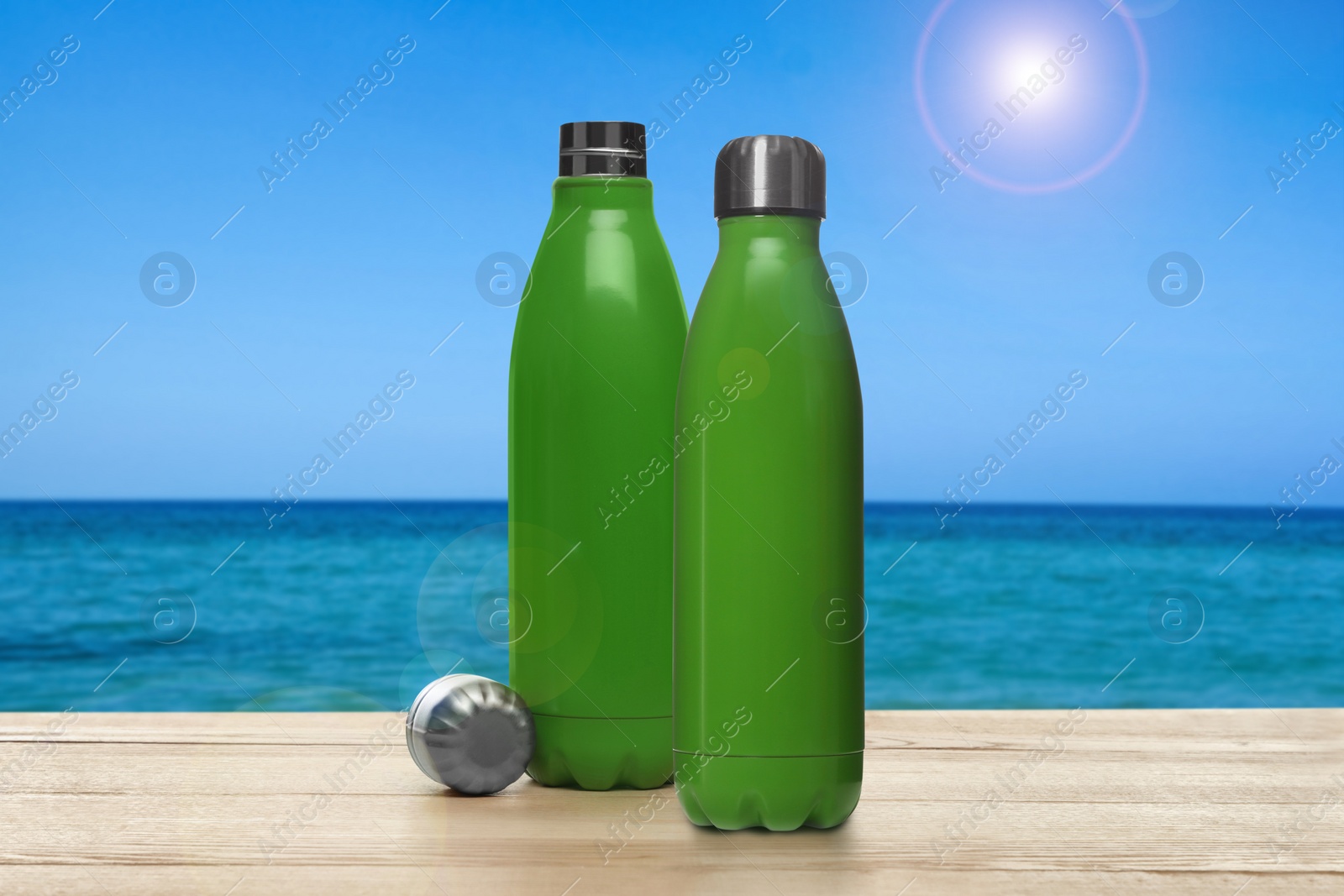 Image of Thermo bottles on wooden table near sea under blue sky
