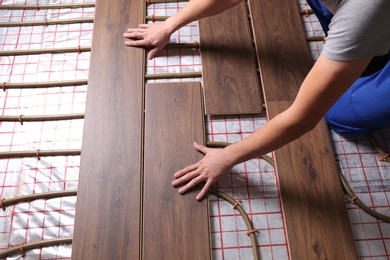 Photo of Worker installing new wooden laminate over underfloor heating system, closeup