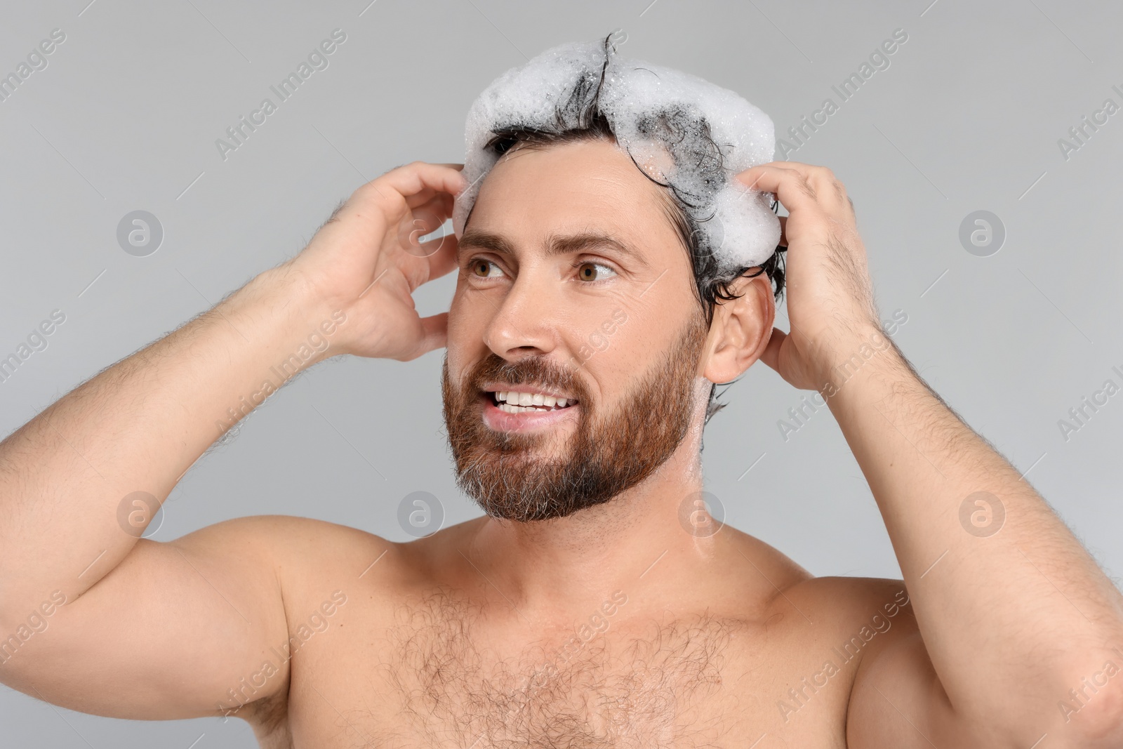 Photo of Happy man washing his hair with shampoo on grey background, closeup