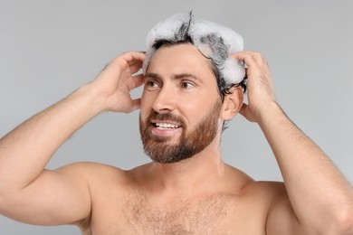 Happy man washing his hair with shampoo on grey background, closeup