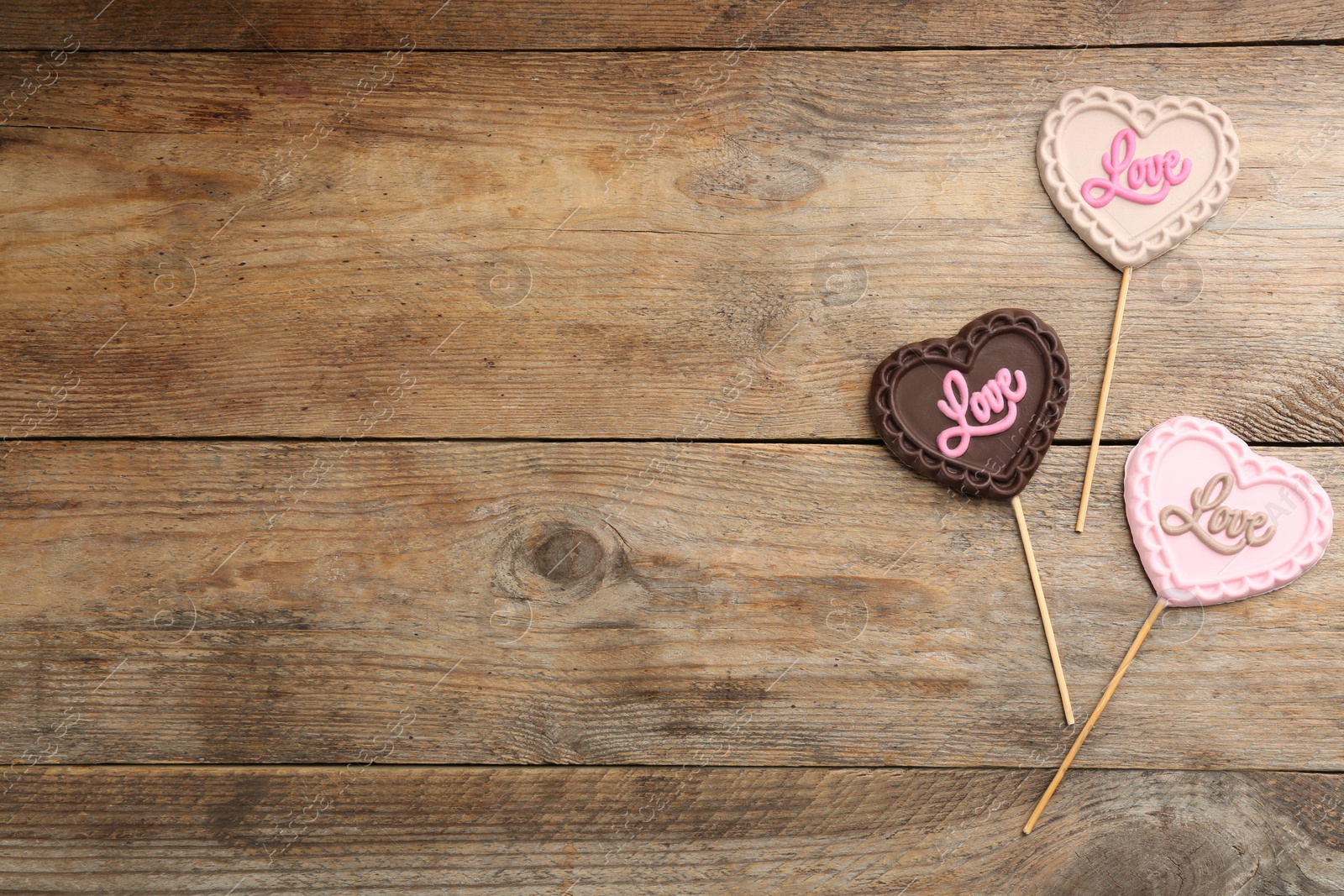 Photo of Different chocolate heart shaped lollipops with word Love on wooden table, flat lay. Space for text