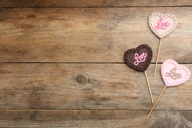 Different chocolate heart shaped lollipops with word Love on wooden table, flat lay. Space for text