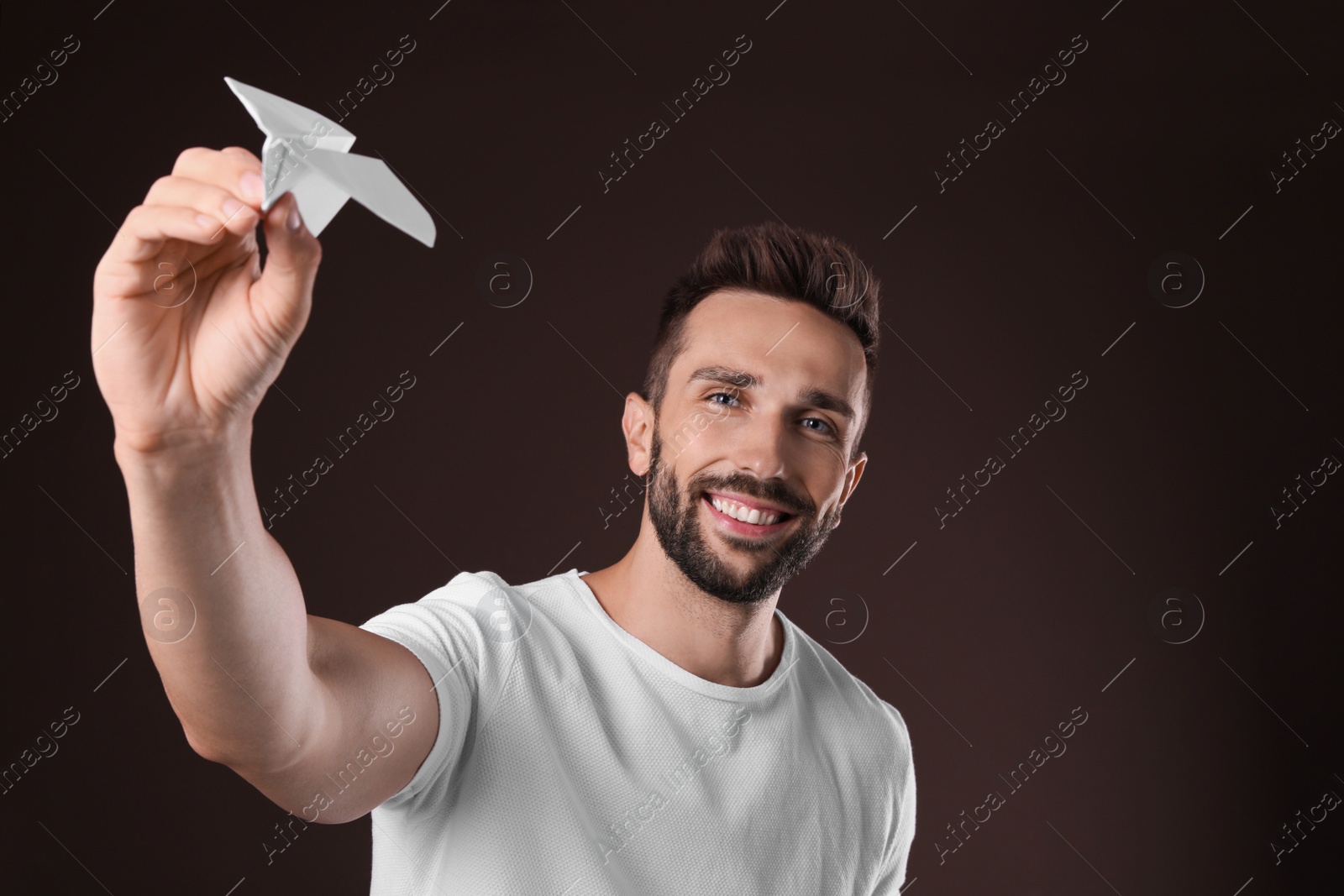 Photo of Handsome man playing with paper plane on brown background