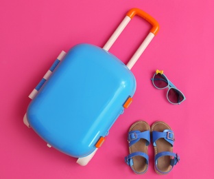 Flat lay composition with suitcase and child accessories on pink background, space for text