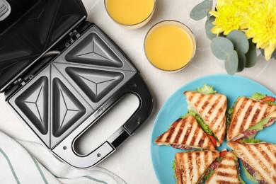 Photo of Modern grill maker, juice and sandwiches on white table, flat lay