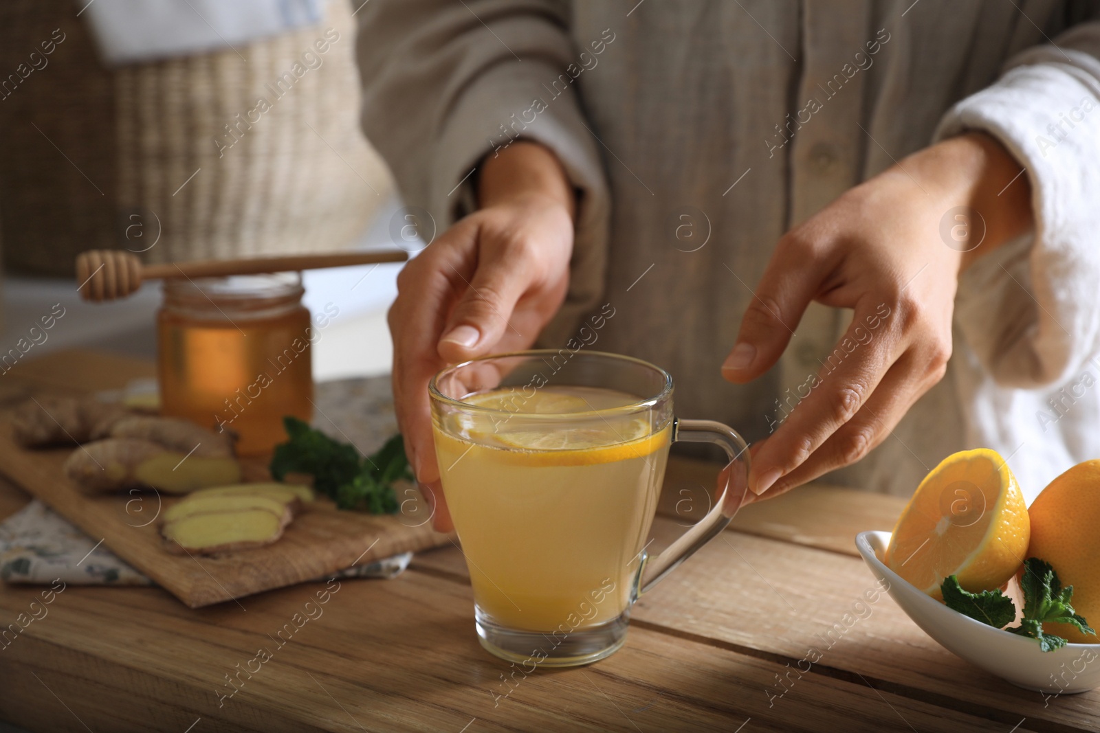 Photo of Woman making aromatic ginger tea at wooden table indoors, closeup