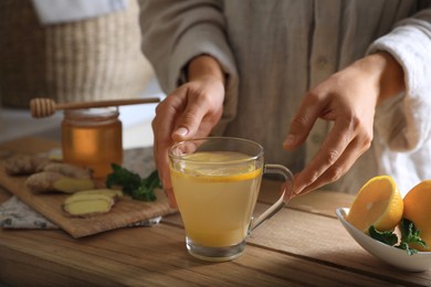Photo of Woman making aromatic ginger tea at wooden table indoors, closeup