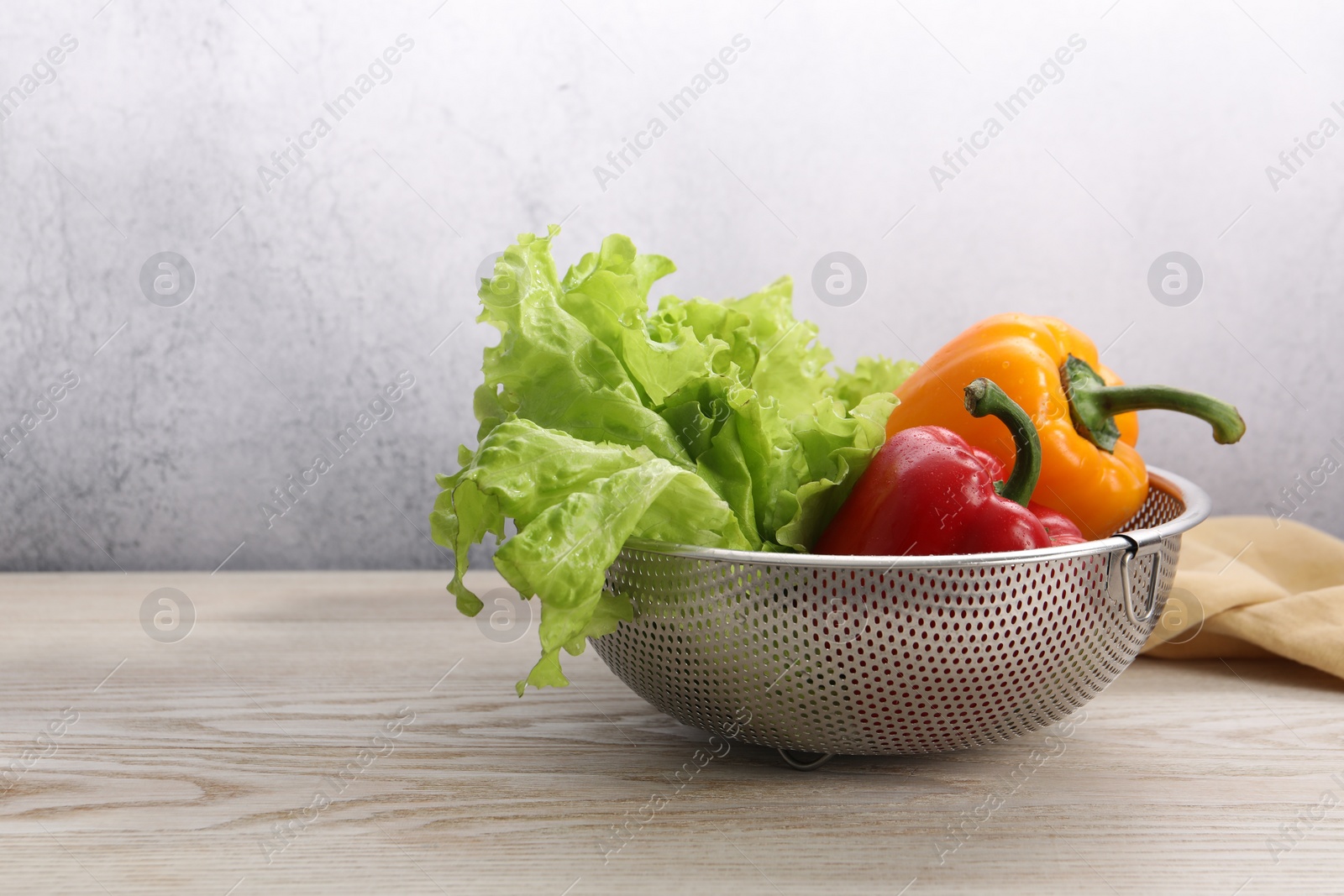 Photo of Colander with fresh lettuce and bell peppers on wooden table, space for text