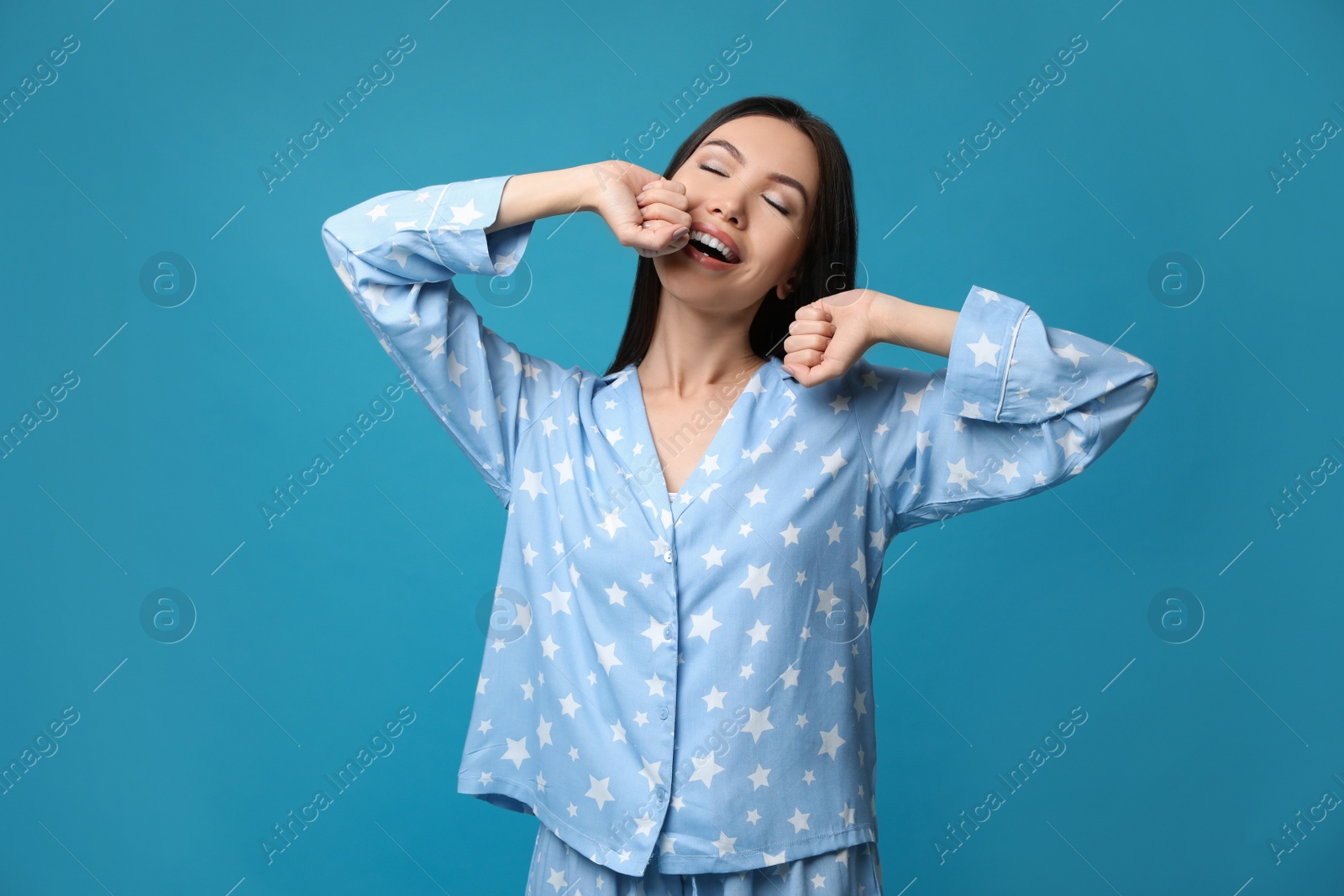 Photo of Beautiful Asian woman in pajamas stretching on blue background. Bedtime