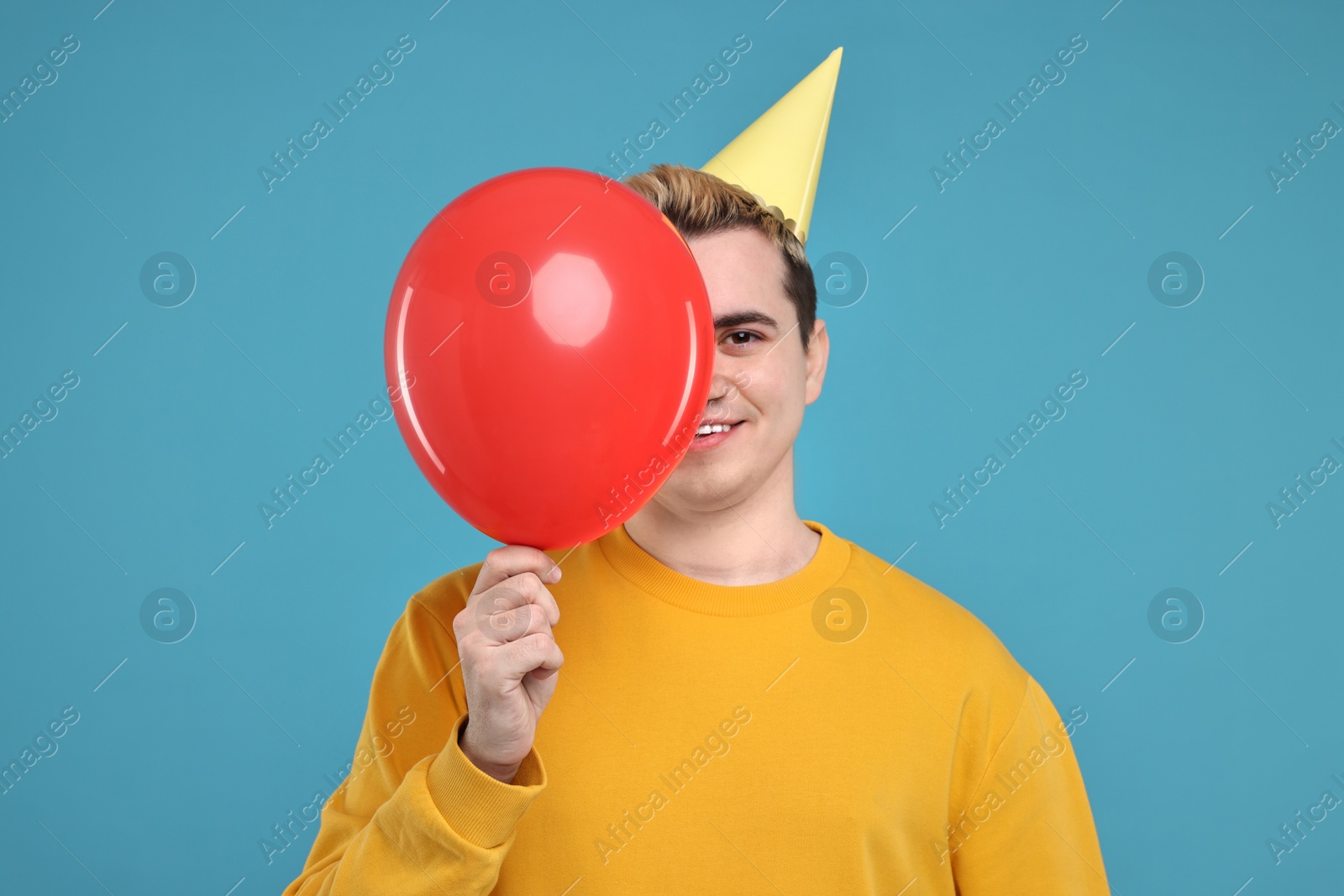 Photo of Young man with party hat and balloon on light blue background