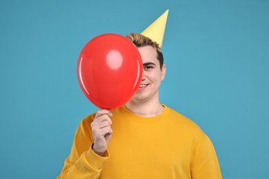 Photo of Young man with party hat and balloon on light blue background