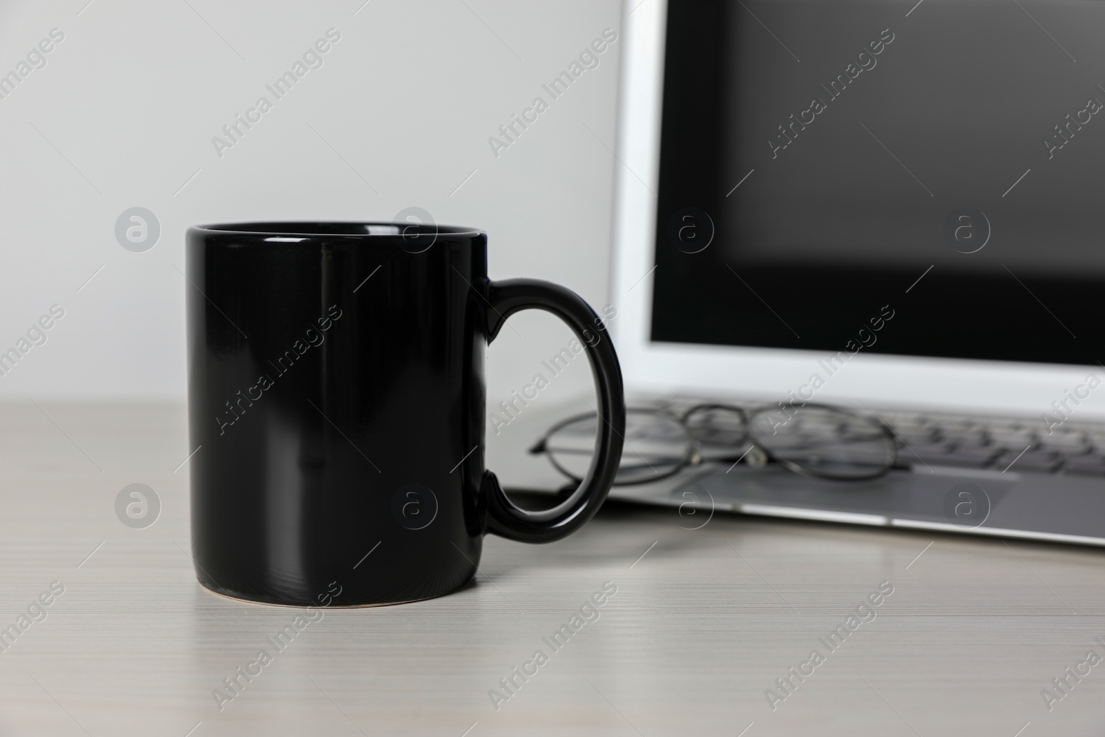 Black ceramic mug, laptop and glasses on white wooden table at workspace Photo of Black ceramic mug, laptop and glasses on white wooden table at workspace