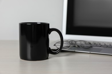 Photo of Black ceramic mug, laptop and glasses on white wooden table at workspace