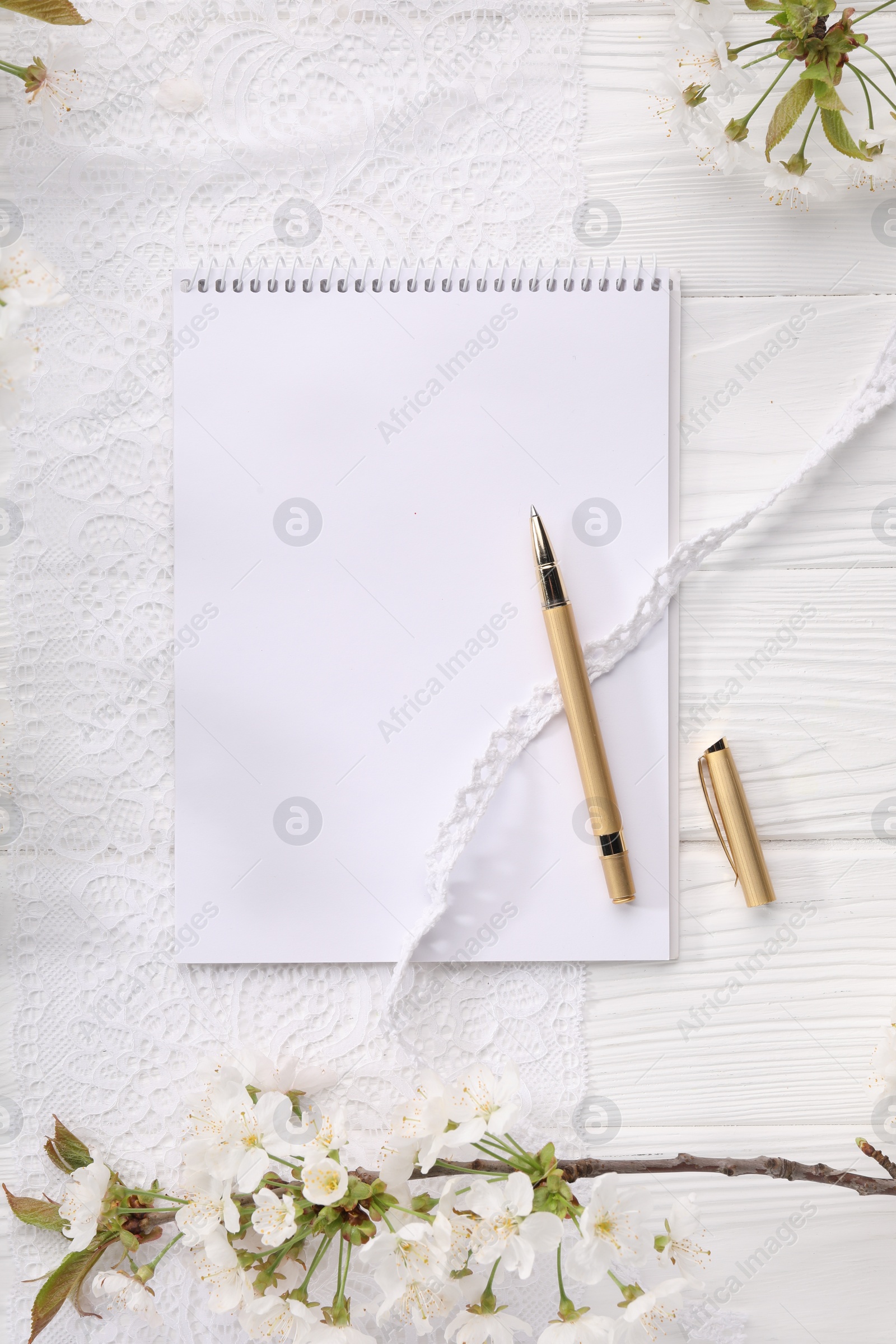 Photo of Guest list. Notebook, pen, spring tree branches with beautiful blossoms and lace ribbons on white wooden background, flat lay