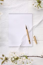 Guest list. Notebook, pen, spring tree branches with beautiful blossoms and lace ribbons on white wooden background, flat lay