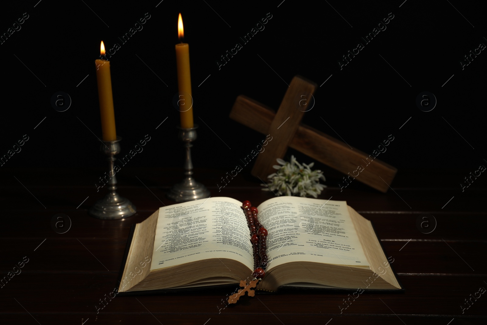 Photo of Crosses, rosary beads, Bible and church candles on wooden table