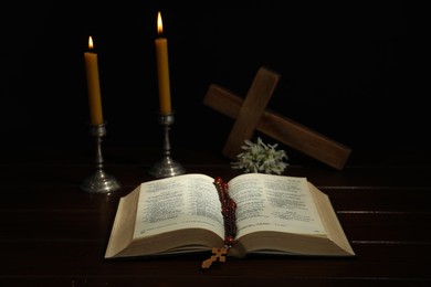 Photo of Crosses, rosary beads, Bible and church candles on wooden table