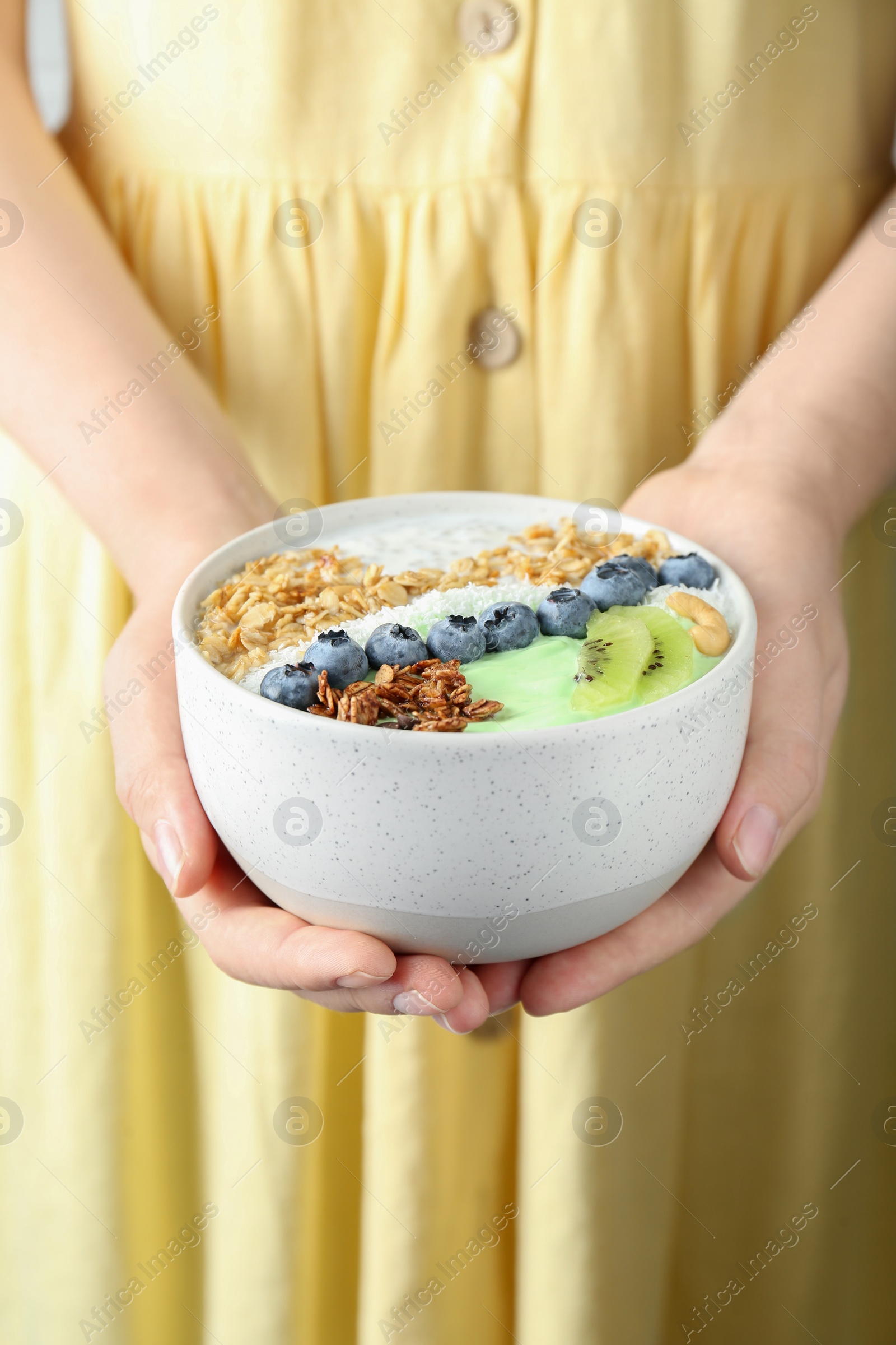 Photo of Woman holding tasty smoothie bowl with fresh kiwi fruit, berries and granola, closeup