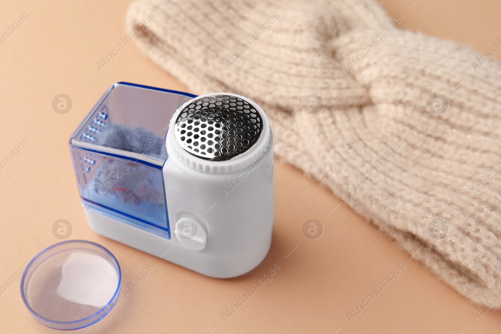 Photo of Modern fabric shaver with fuzz and knitted headdress on pale orange background, closeup. Space for text