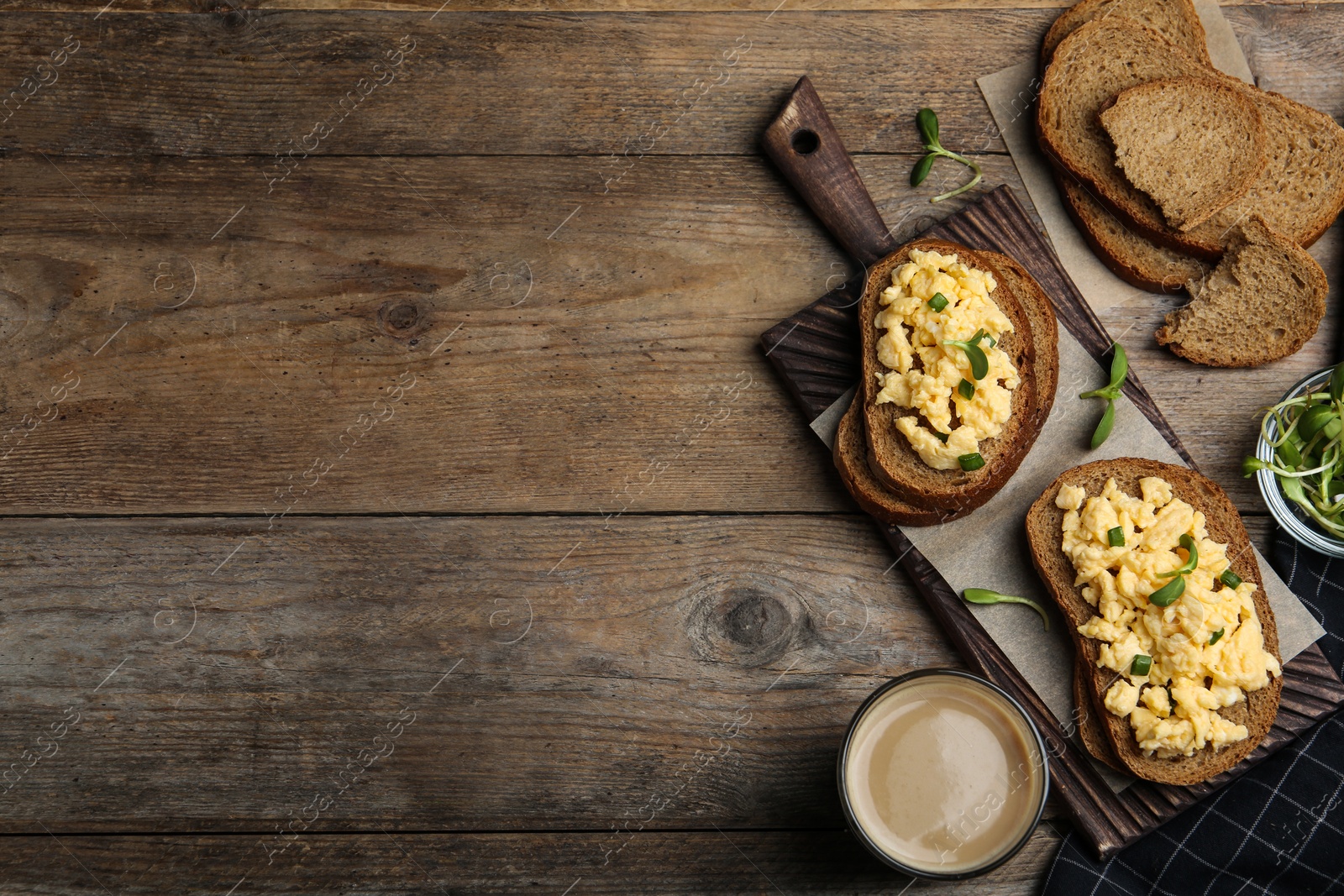 Photo of Tasty scrambled egg sandwiches served on wooden table, flat lay. Space for text