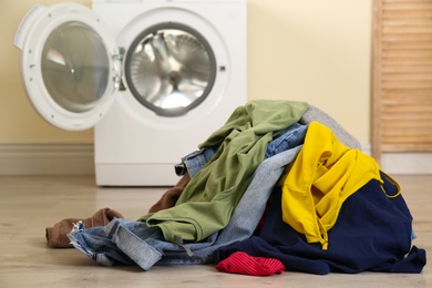 Pile of dirty laundry near washing machine indoors