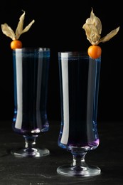 Refreshing cocktails decorated with physalis fruits on grey table against black background