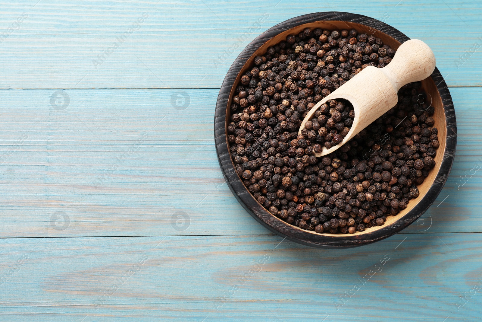 Photo of Aromatic spice. Black pepper in bowl and scoop on light blue wooden table, top view. Space for text