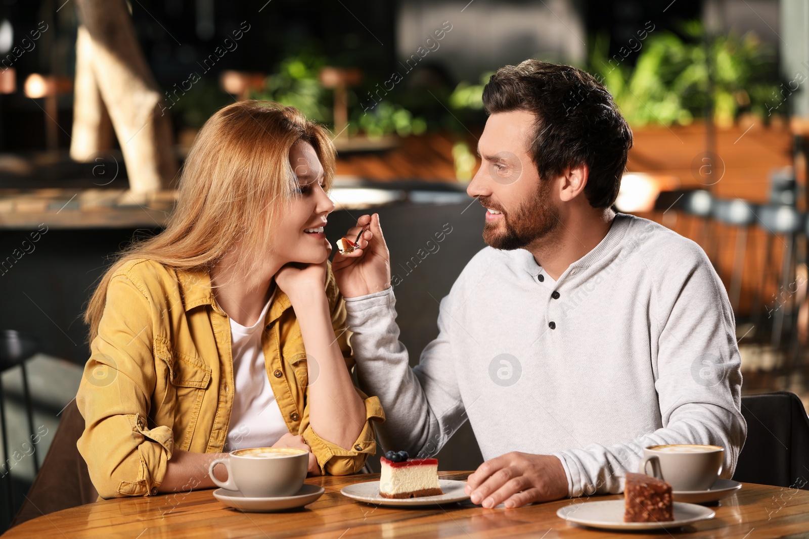 Photo of Romantic date. Handsome man feeding his girlfriend with cake in cafe