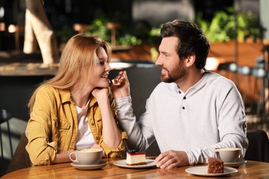 Photo of Romantic date. Handsome man feeding his girlfriend with cake in cafe