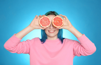 Photo of Young woman with bright dyed hair holding grapefruit on light blue background