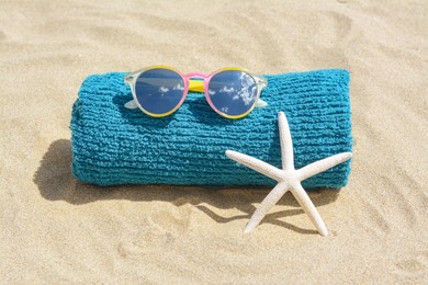 Towel, stylish sunglasses and starfish on sand outdoors. Beach accessories
