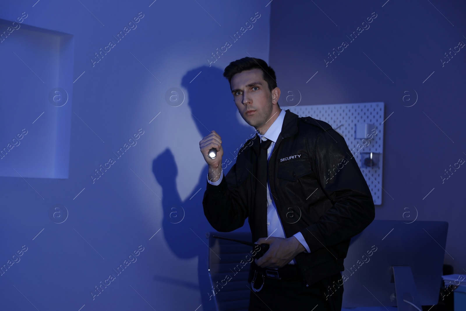 Photo of Male security guard with flashlight and portable radio transmitter in dark room