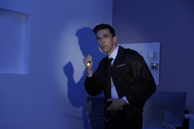 Photo of Male security guard with flashlight and portable radio transmitter in dark room