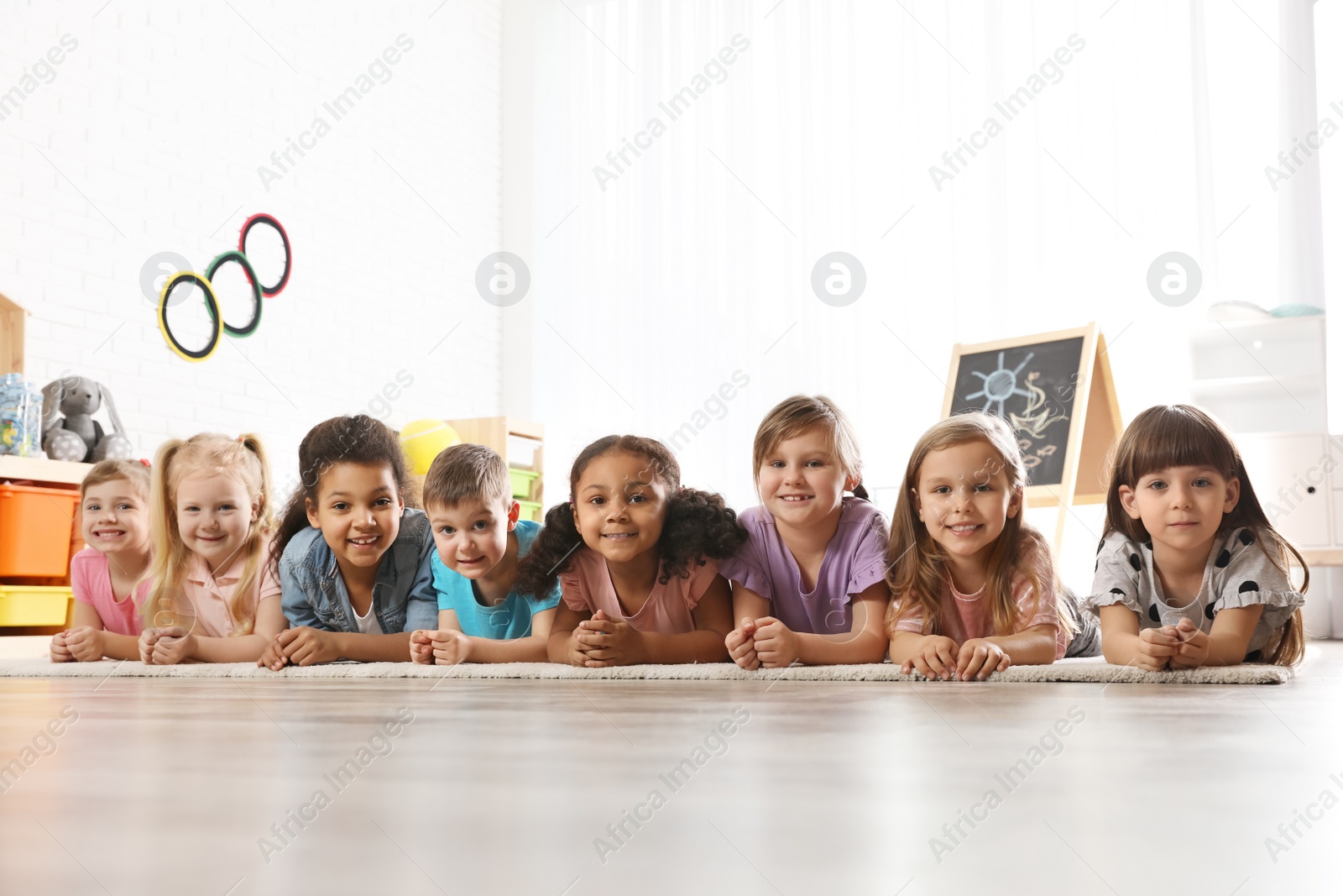 Photo of Group of cute little children lying on floor indoors. Kindergarten playtime activities