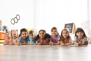 Photo of Group of cute little children lying on floor indoors. Kindergarten playtime activities